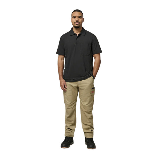 Man wearing Hard Yakka Legends Slim Fit Stretch Work Pants, featuring multiple utility pockets and a slim, articulated fit, paired with a black polo shirt and black lace-up boots.