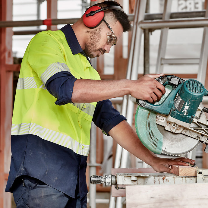 Syzmik Hi Vis Outdoor Segmented Tape L/S Shirt: Man in safety gear using a circular saw, showcasing breathable, lightweight workwear with segmented tape and roll-up sleeves, ideal for comfort and mobility in active safety environments.